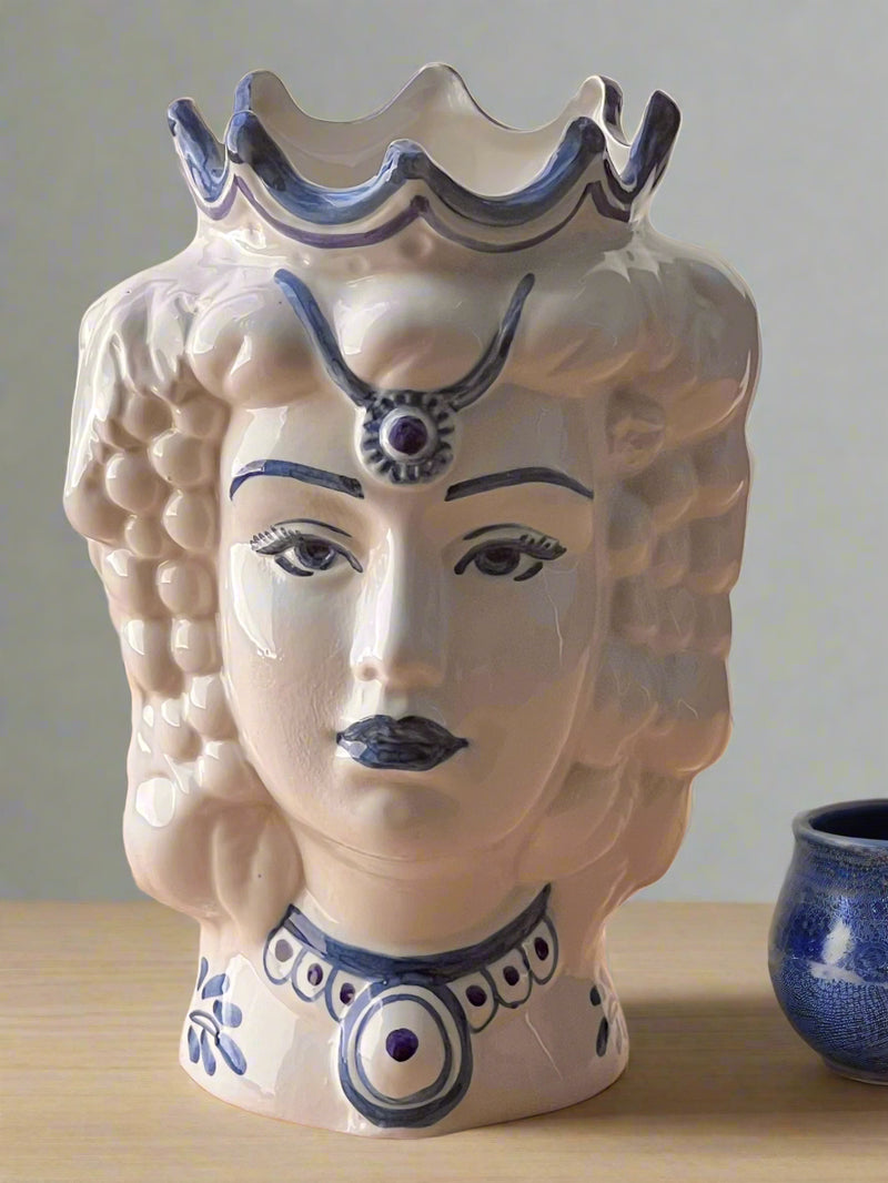 Ceramic vase shaped like a woman's face with blue decorative elements on a wooden surface.