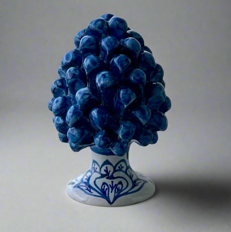 Decorative pine cone with handpainted blue and white bird of paradise design on a white base against a light gray background