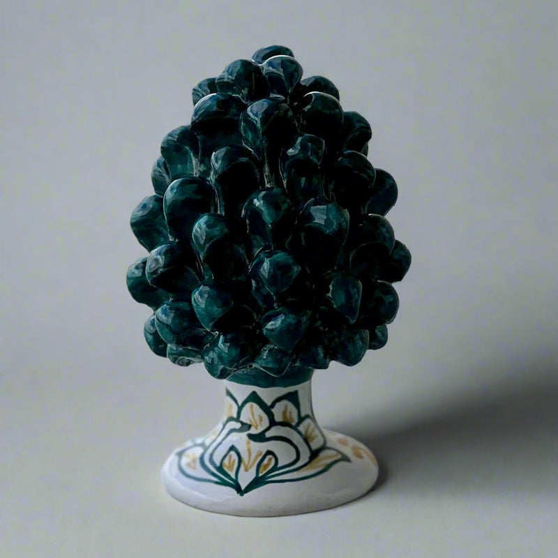 Decorative pine cone on a white base with hand painted green bird of paradise pattern.