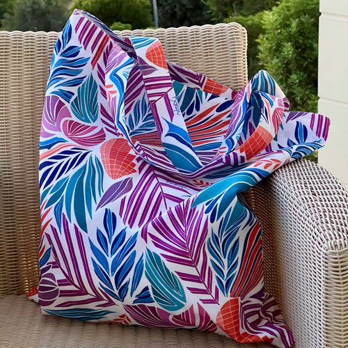 Colorful Drifting Leaf patterned waterproof tote bag draped over a wicker chair outdoors.