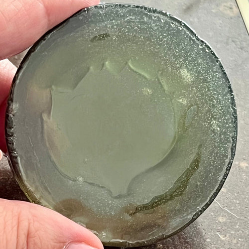 Hand holding a green round soap bar on a dark background
