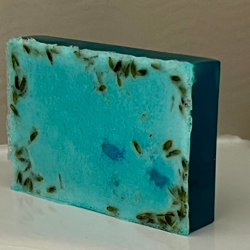 Blue and green soap bar with lavender buds on a white surface