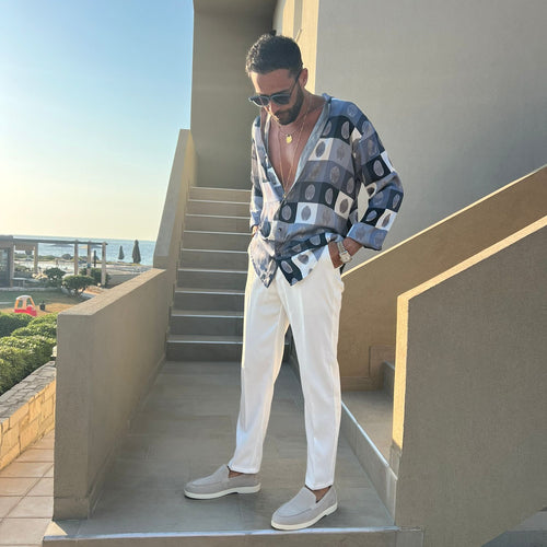 Man in a patterned shirt and white pants standing on steps outdoors.