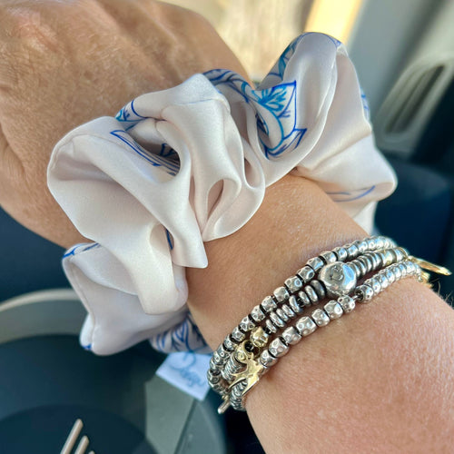 Close-up of a wrist wearing a white scrunchie with blue patterns and multiple bracelets.