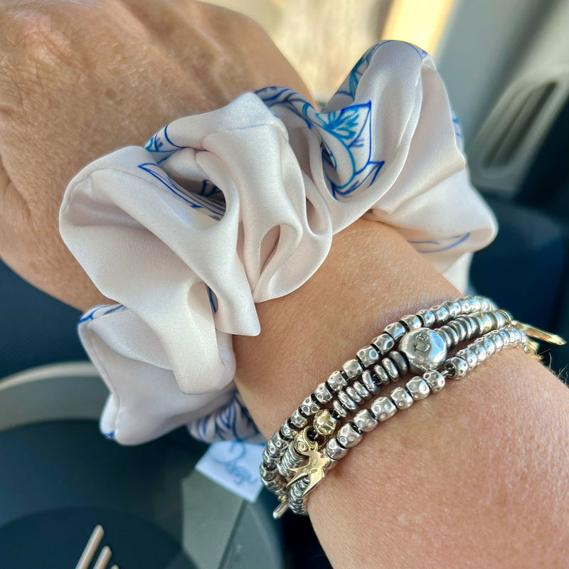 Close-up of a wrist wearing a white scrunchie with blue patterns and multiple bracelets.